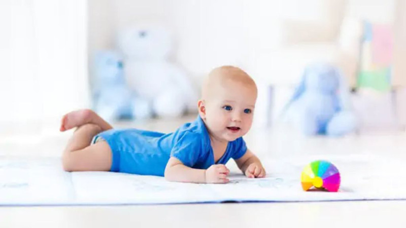 Bé đang với tay lấy đồ chơi, khuyến khích kỹ năng trườn bò